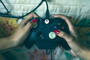 A hand with red nails holding an Xbox Controller.